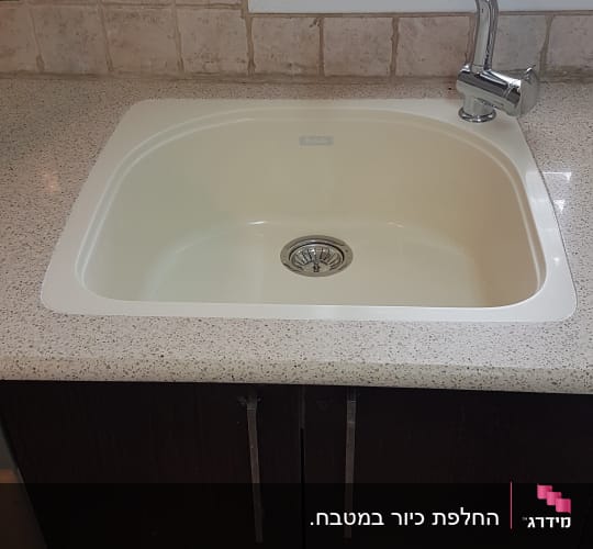 התקנת כיור מטבח בתוך משטח שיש בהיר מעל ארונות כהים